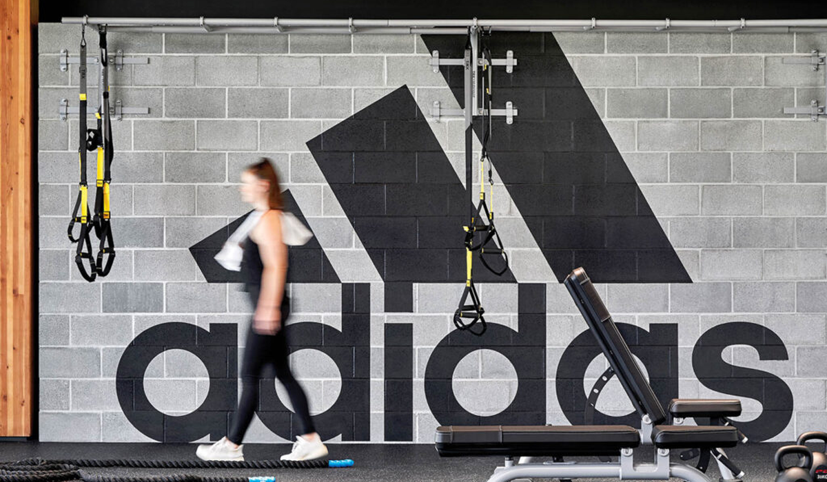Woman walking past wall with adidas branding on it