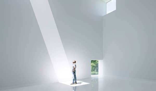 sunlight streams through an aperture in the ceiling in an all white gallery room