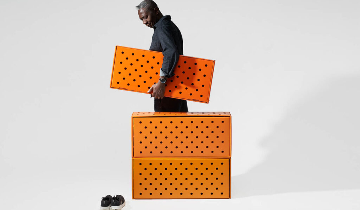 a man carries a bright orange shoebox with black polka dots