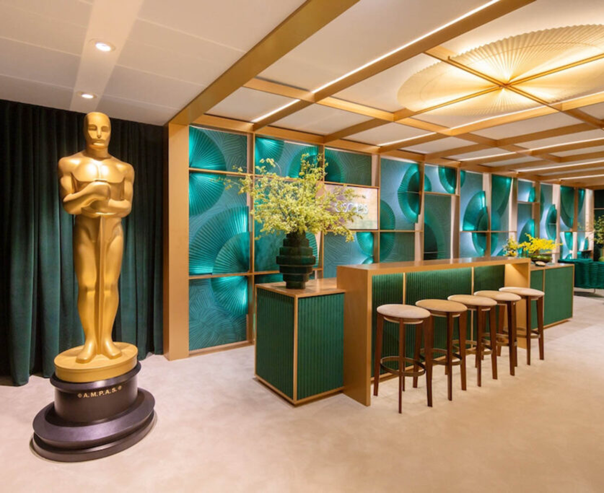 Giant golden Oscars statue next to bar with green panels and plants