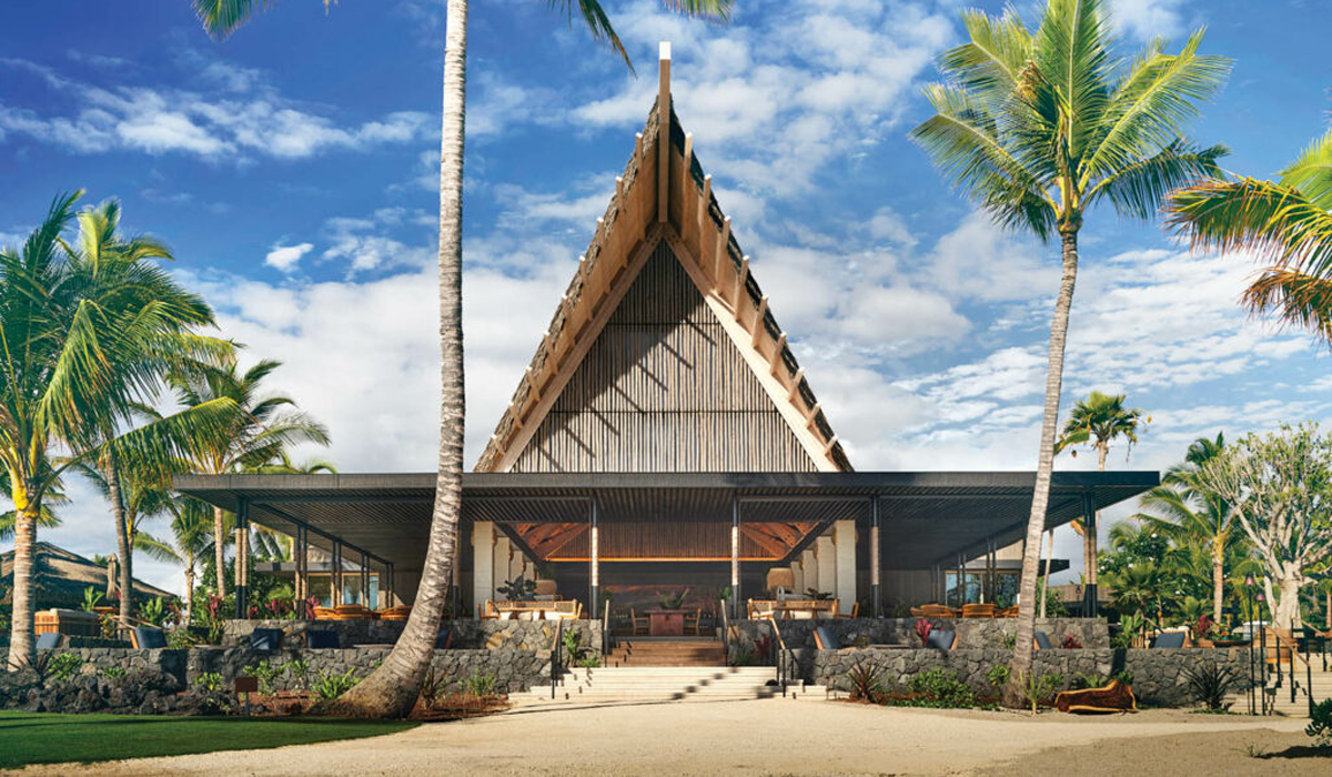 exterior facade of Hawaiian resort with large pointed roof and palm trees all around