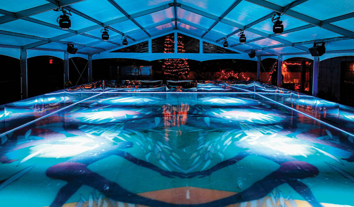 ice rink with a figure skating installation and mural below the ice and Christmas trees in background