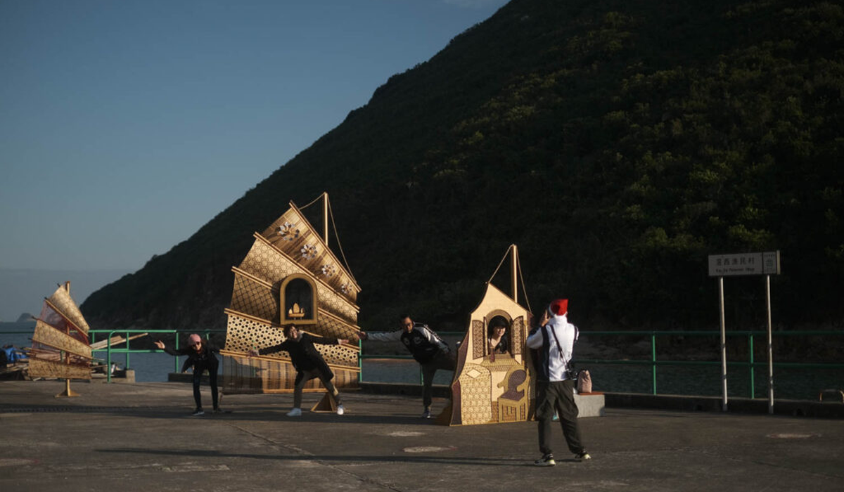 people posing by wooden cutouts that resemble boats by the pier