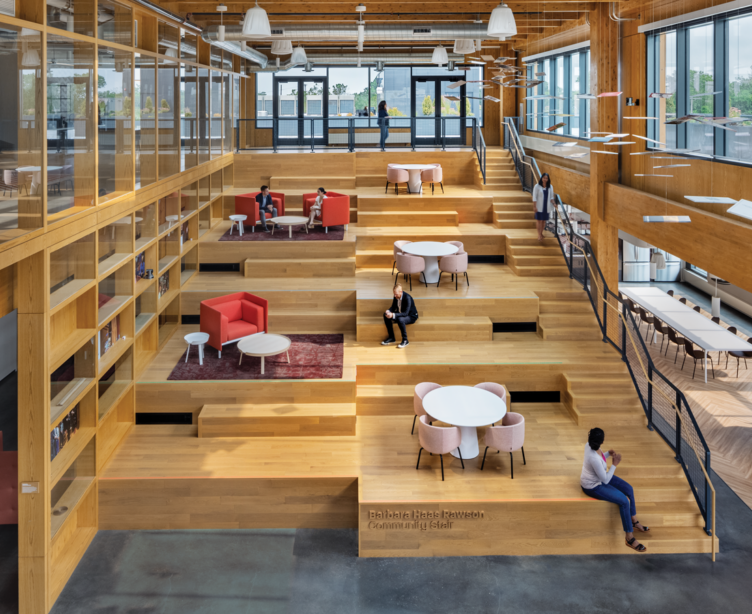 large communal space with people sitting on top of wooden platforms with windows all around