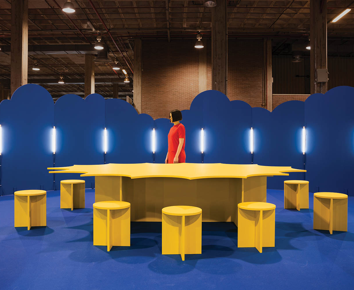 woman in red standing in front of yellow table amidst blue clouds