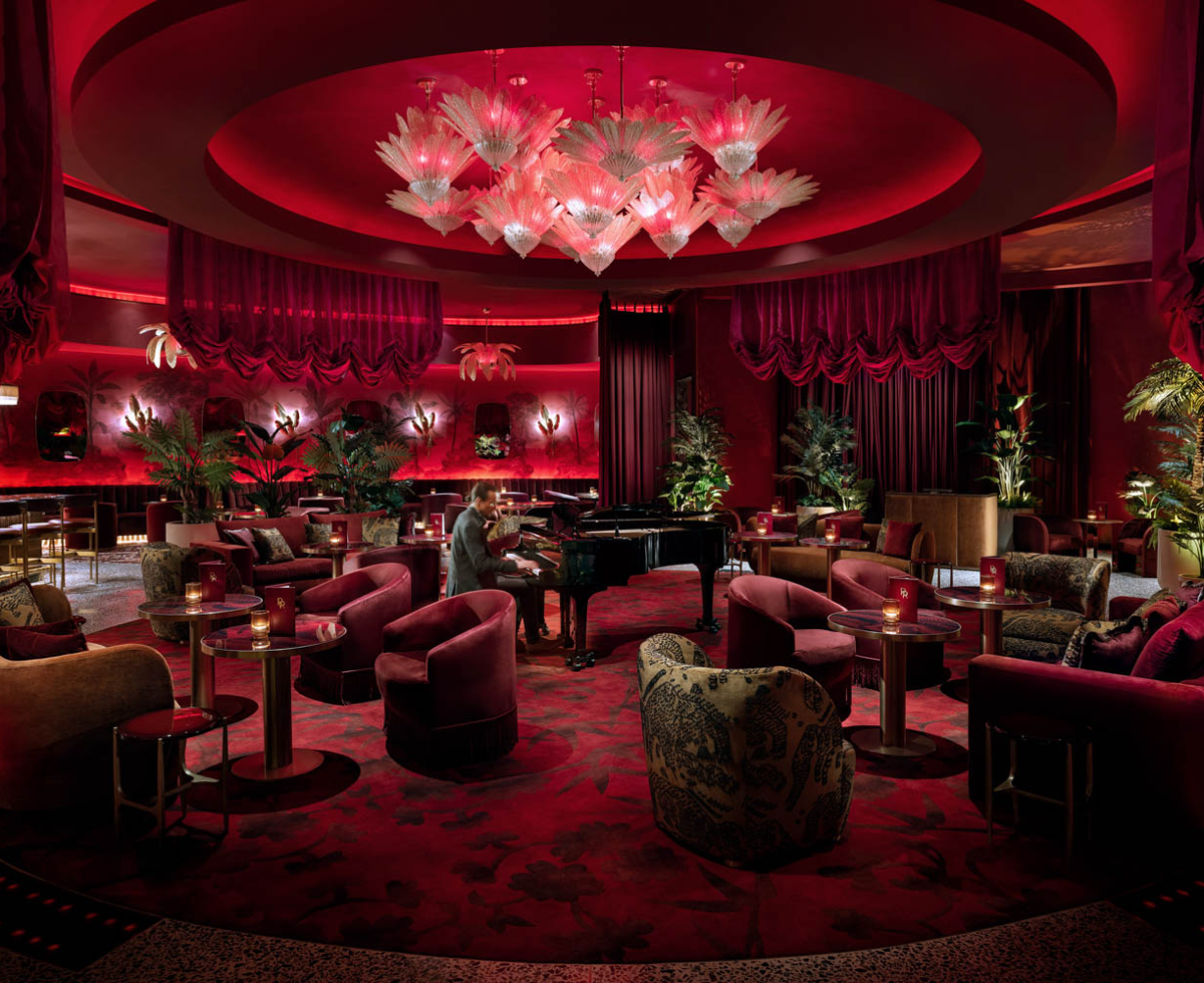 all red cocktail lounge with multiple chairs, piano player and chandeliers