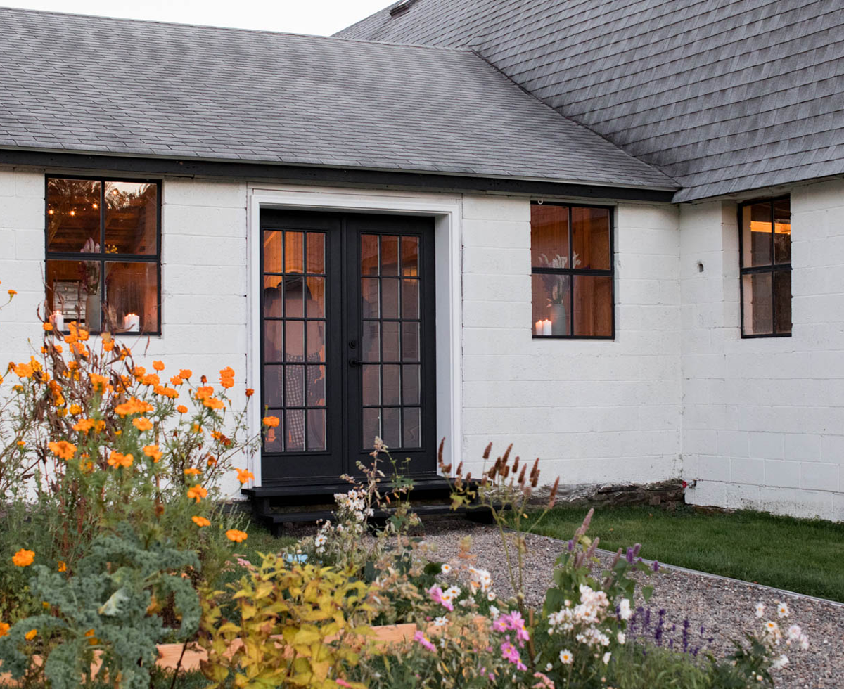 exterior of white farmhouse with wildflowers