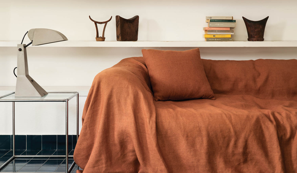 corner of room with orange sheet over a couch and in front of white bookshelf