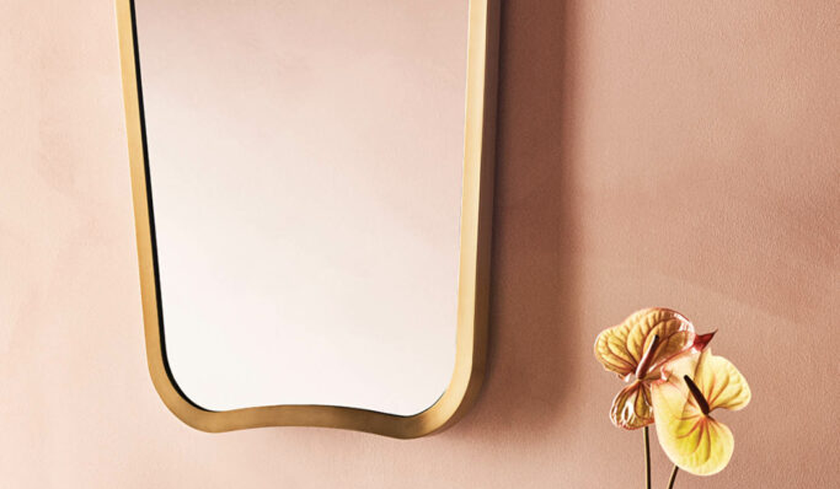 a caged brass vanity mirror against a peach wall