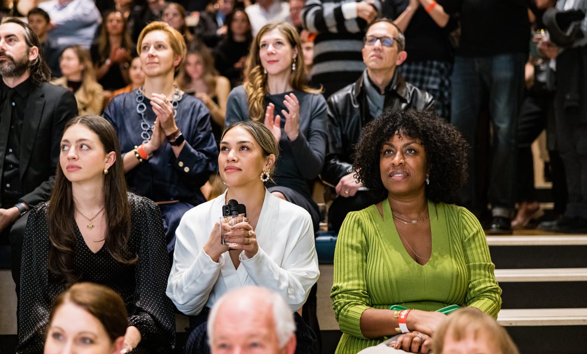 People sitting on tiered seating clapping at an event and looking at a speaker off camera