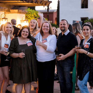 A group of people with name tags and holding drinks posing for a group photo at an event.